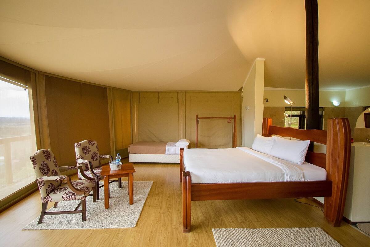 A hotel room with a wooden bed, a sofa bed, two armchairs, a small table, and a large window.
