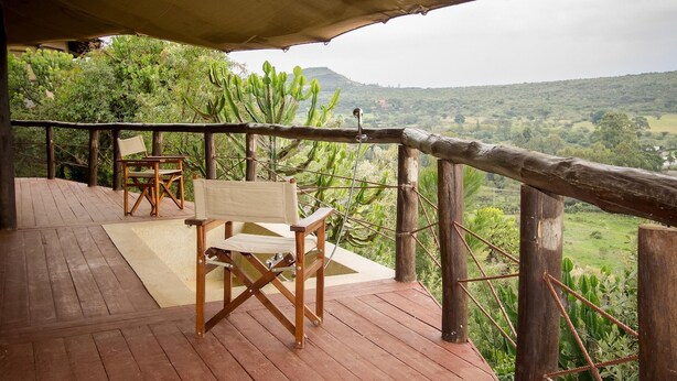 Une terrasse en bois avec une chaise et une table en bois, offrant une vue sur un paysage composé de cactus et de collines.