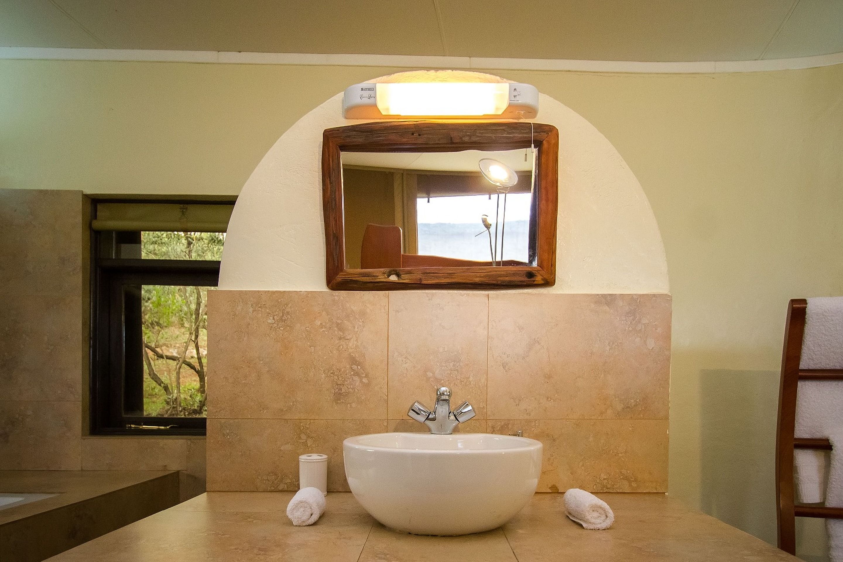 A bathroom with a large sink, a mirror above it, and a window with a view of trees.
