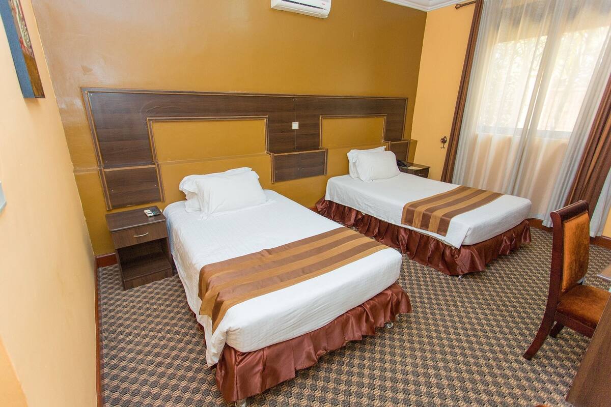 A hotel room with two beds, a wooden headboard, a patterned carpet, and a window with curtains.