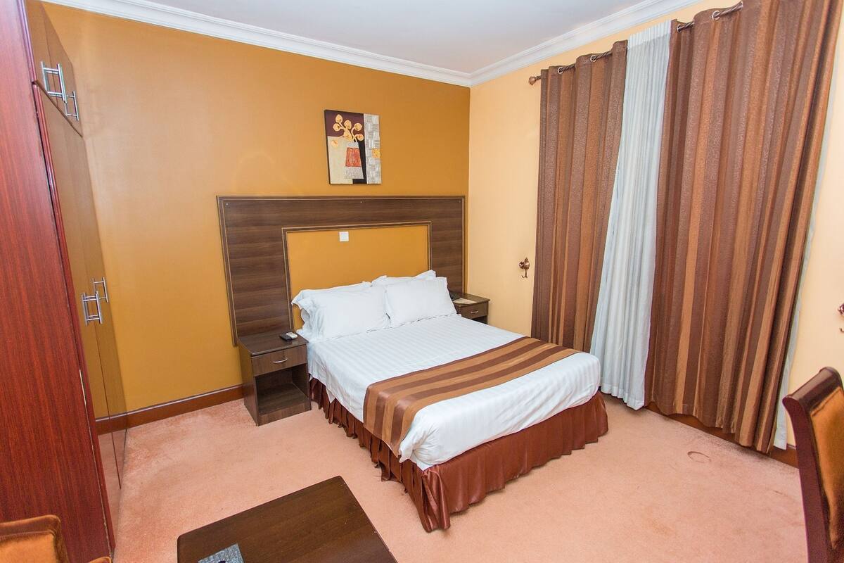 A hotel room with a large bed, a wooden headboard, a nightstand, a desk, and a chair.