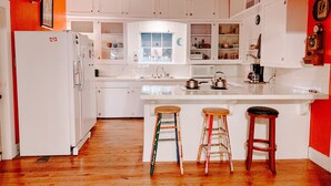 Una cocina con armarios blancos, piso de madera y tres taburetes.