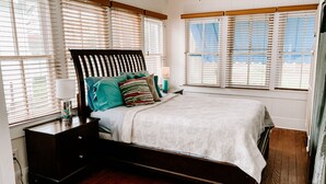 Un dormitorio con cama, mesitas de noche y una ventana con persianas.