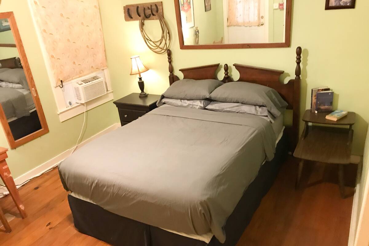 Un dormitorio con cama, mesita de noche, lámpara, espejo y aire acondicionado instalado en la pared.