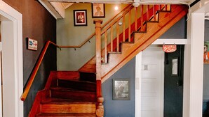 Una escalera de madera con barandilla, una puerta con un cartel, y una pared con cuadros y un póster.