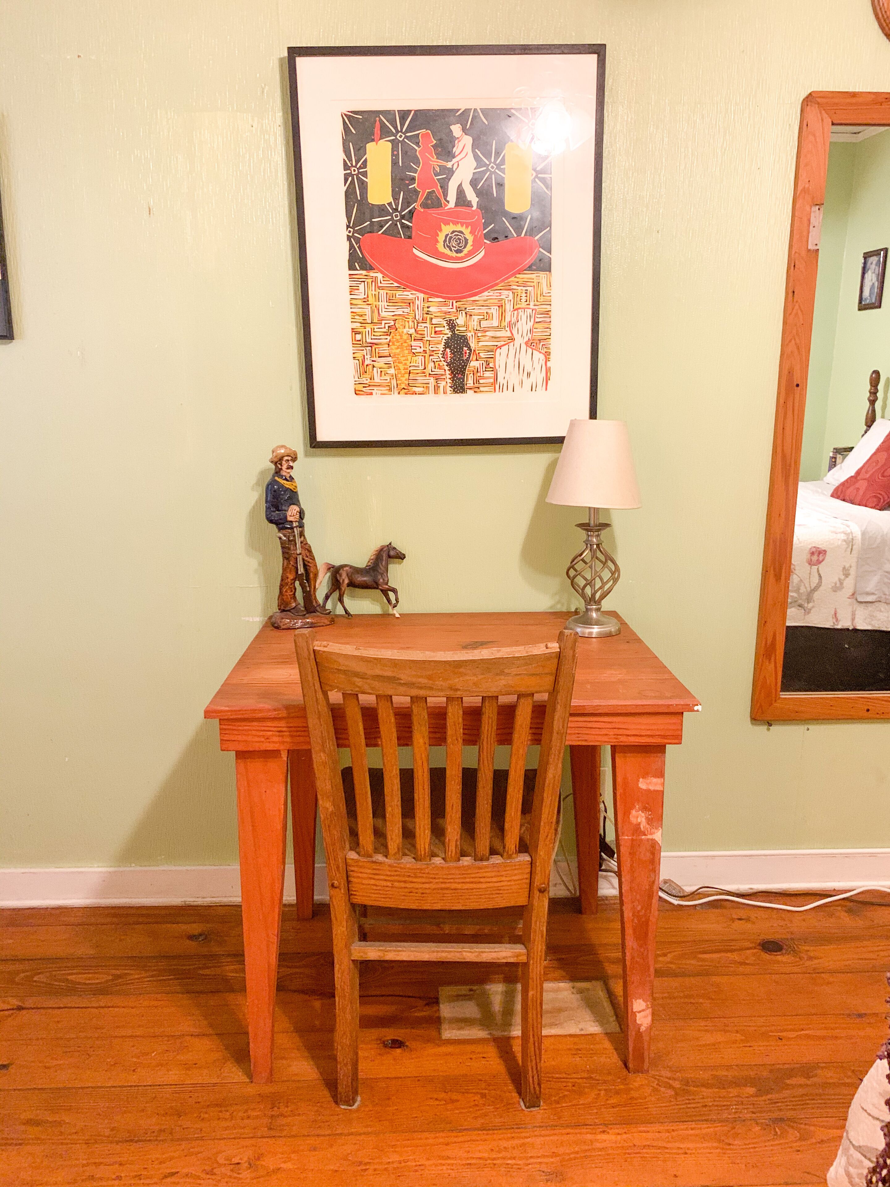 A wooden desk with a chair, a framed artwork above it, a small lamp, and a decorative horse figure.