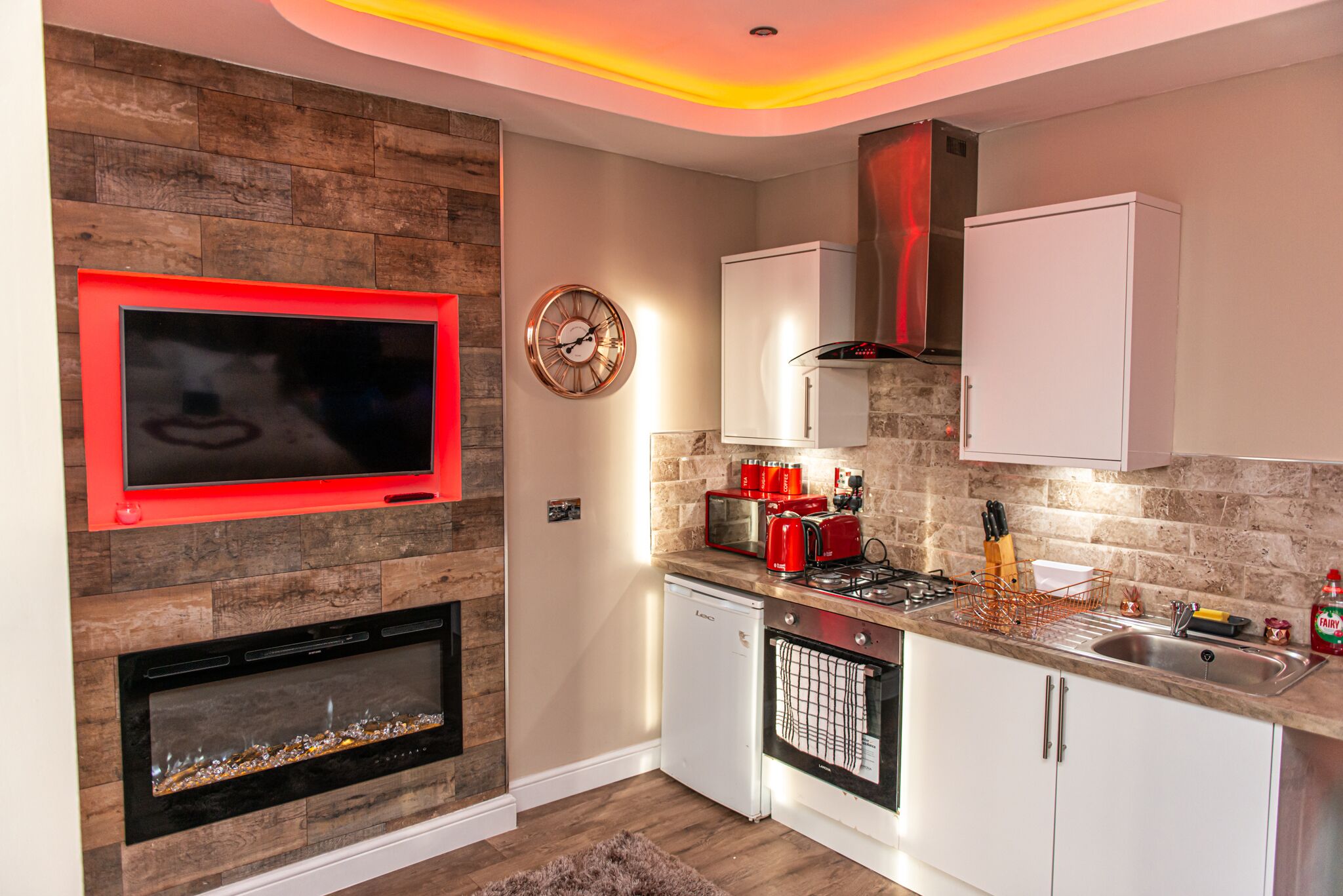 A modern kitchen with a built-in fireplace, a clock, and a red-framed TV.