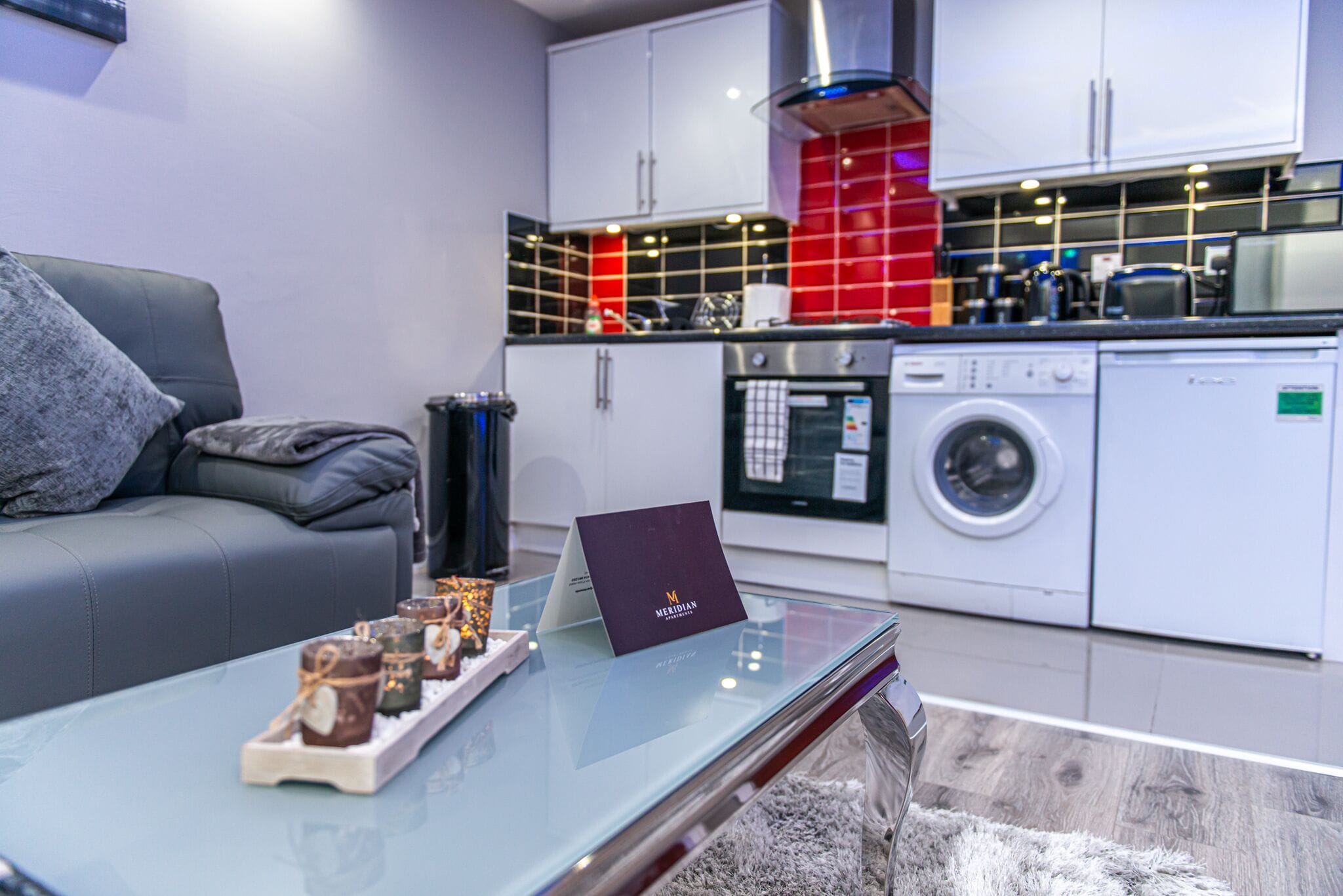 A modern kitchen with white cabinets, a red backsplash, and a glass coffee table with candles.