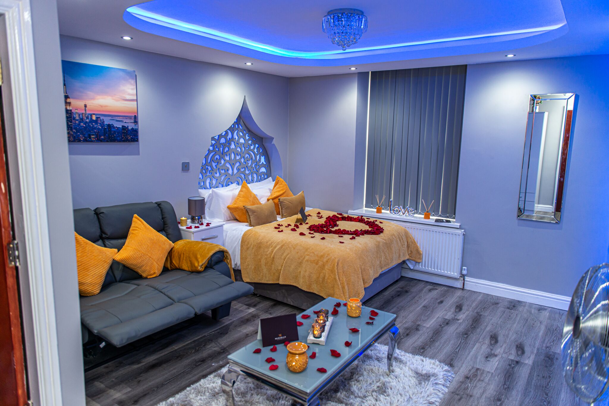 A modern bedroom with a bed, sofa, and a table with rose petals and candles.