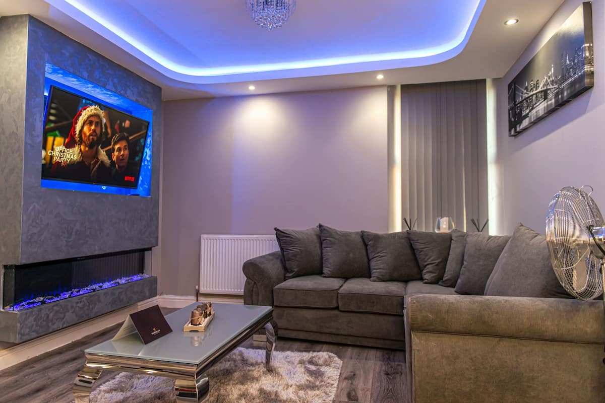 A modern living room with a flat-screen TV, a fireplace, a sofa, and a fan.