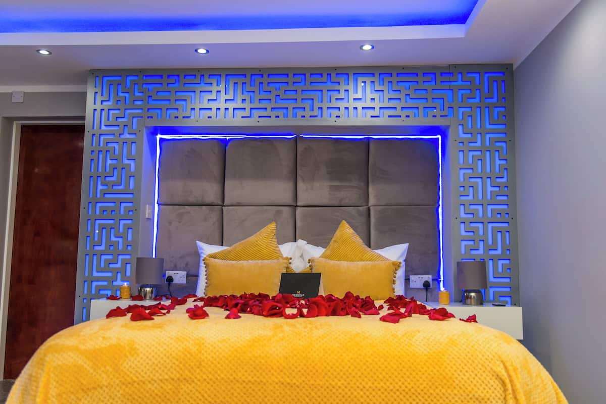 A modern bedroom with a tufted headboard, decorative wall panels, and a bed adorned with rose petals and golden pillows.