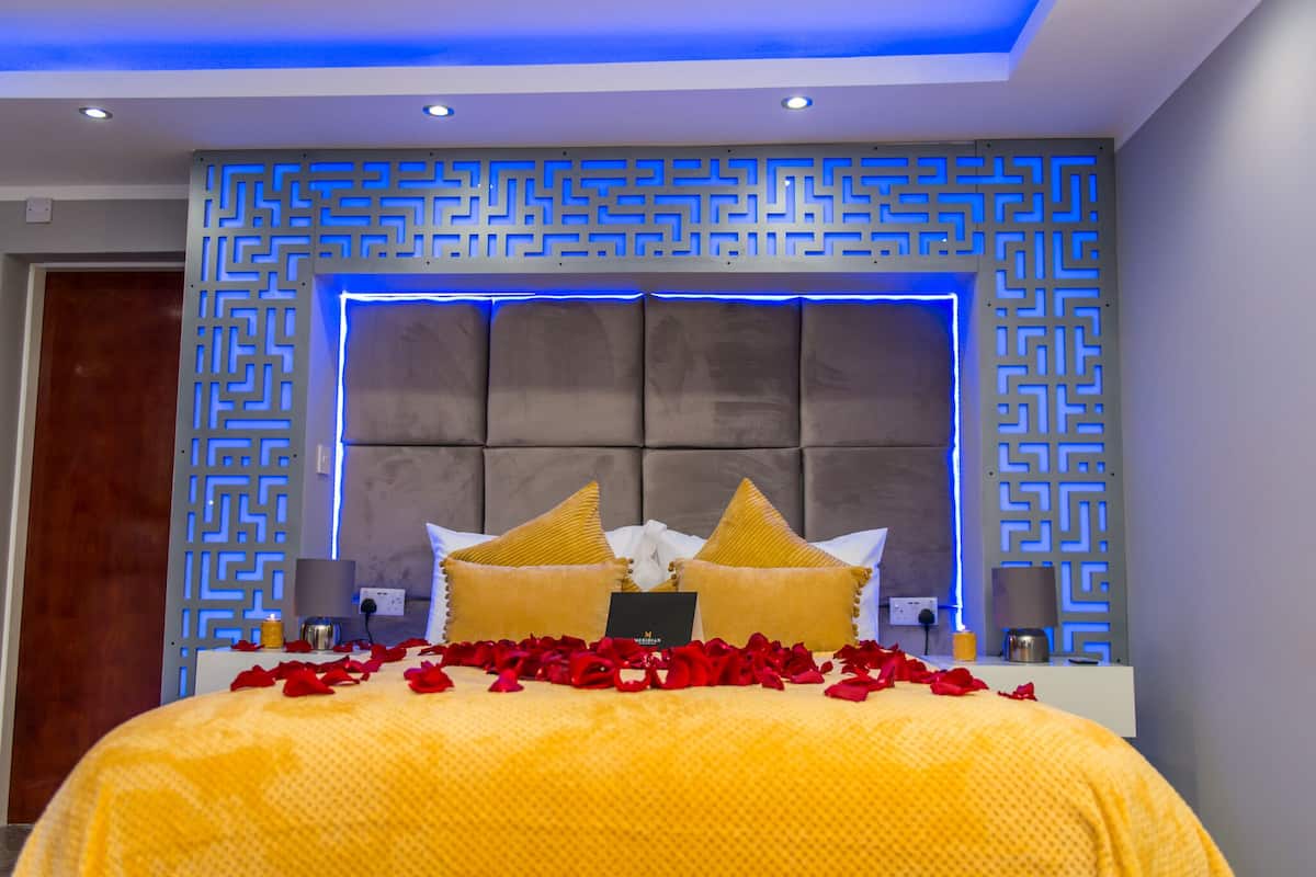 A modern bedroom with a tufted headboard, decorative wall panels, and a bed adorned with rose petals and golden pillows.