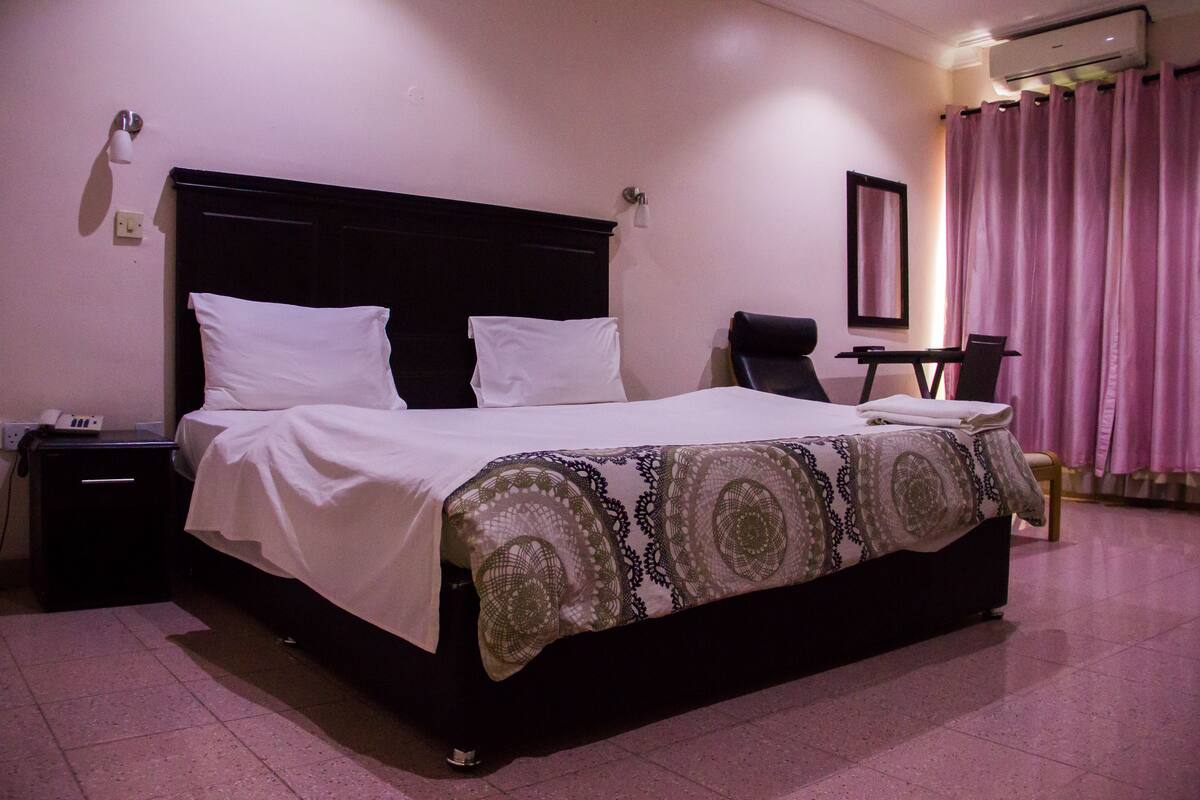A neatly made bed with a patterned bedspread, a bedside table with a lamp, and a chair in a hotel room.
