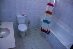 A bathroom with a toilet, sink, shower curtain, and bathtub. - Lekki Heights Hotel (Lekki)