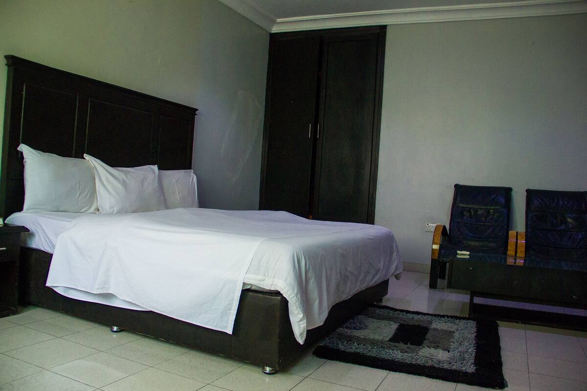 A neatly made bed with white linens, a dark headboard, and a small bedside table with a lamp.