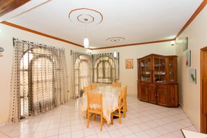 A dining area with a table and chairs, a cabinet with glass doors, and a ceiling with a circular design. - Eden Escape Villa (Kigali)