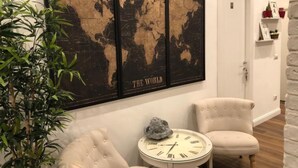Una stanza con una grande mappa del mondo appesa al muro, due poltrone imbottite, un tavolino rotondo con un orologio e una pianta in vaso.