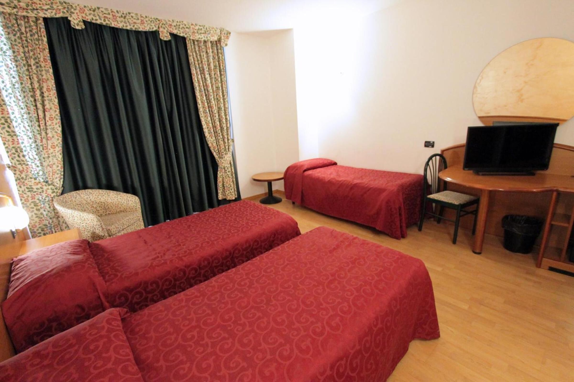 A hotel room with two single beds, a desk with a laptop, a chair, a small table, and a large mirror.
