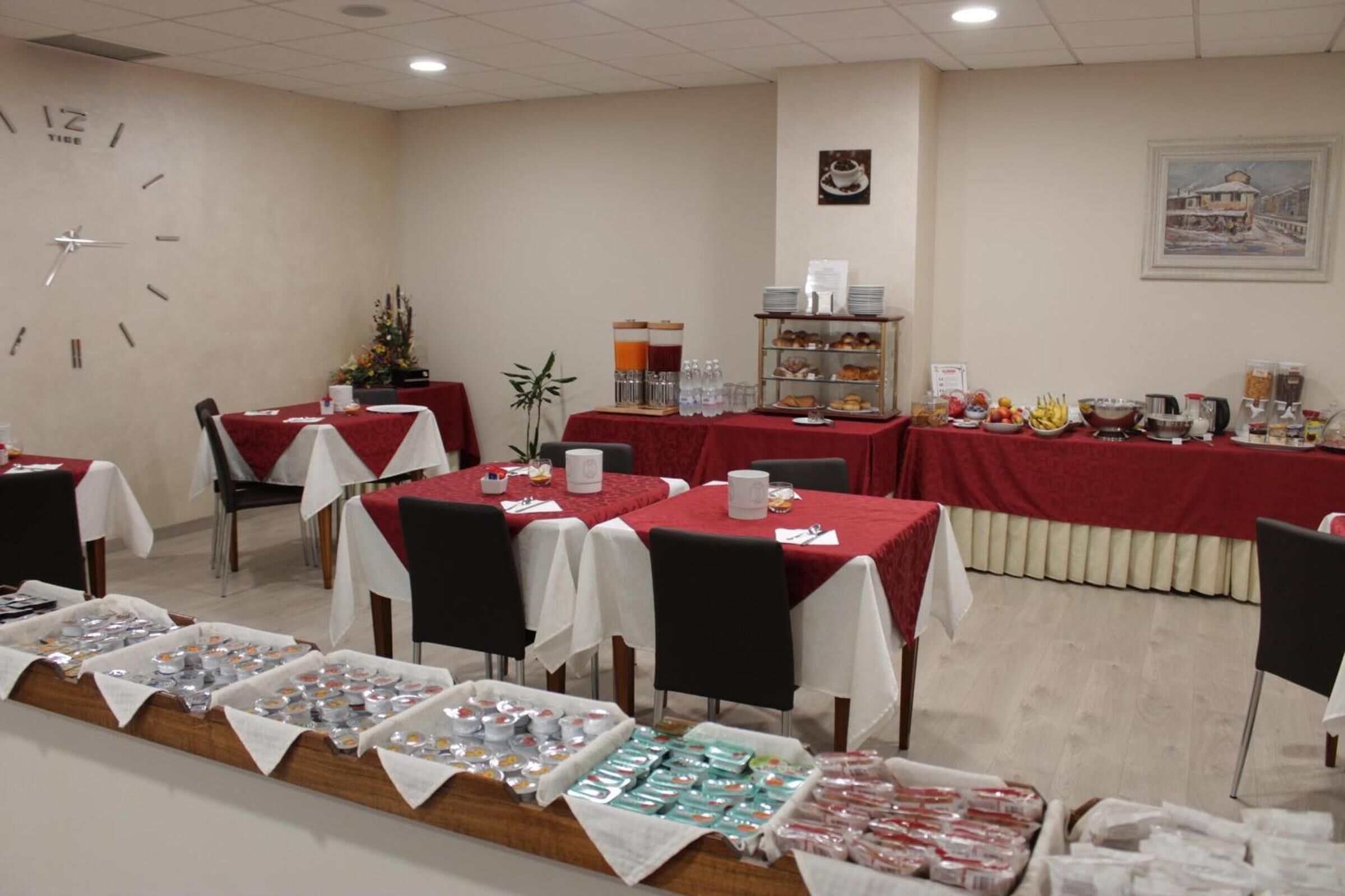 Un salón de conferencias con mesas cubiertas con manteles rojos, equipado con sillas, un reloj y varias estaciones de comida y bebidas.