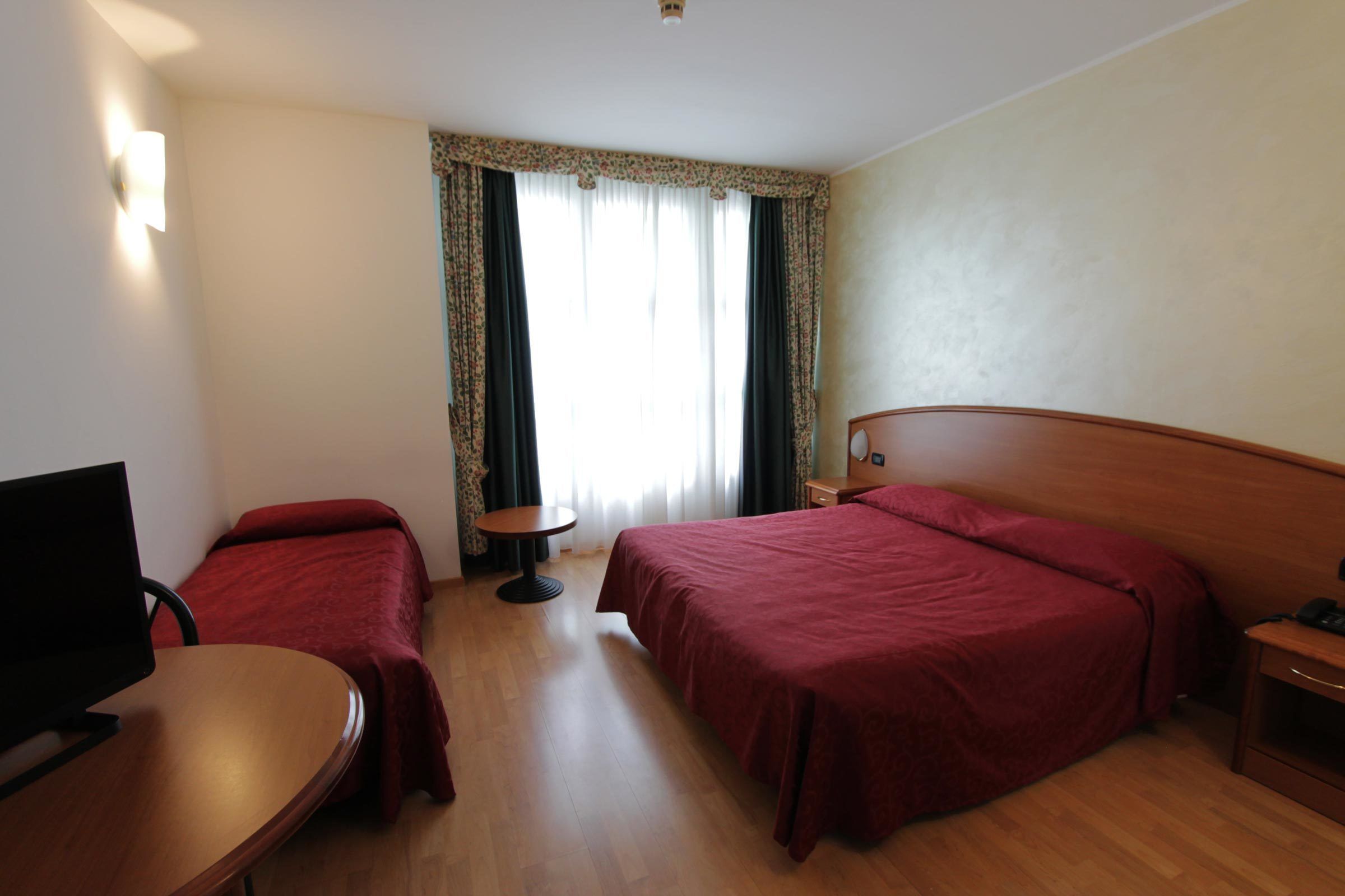 Habitación de hotel con dos camas, un escritorio, una silla, un televisor y una ventana con cortinas.