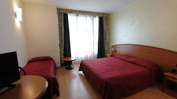 Habitación de hotel con dos camas, un escritorio, una silla, un televisor y una ventana con cortinas.