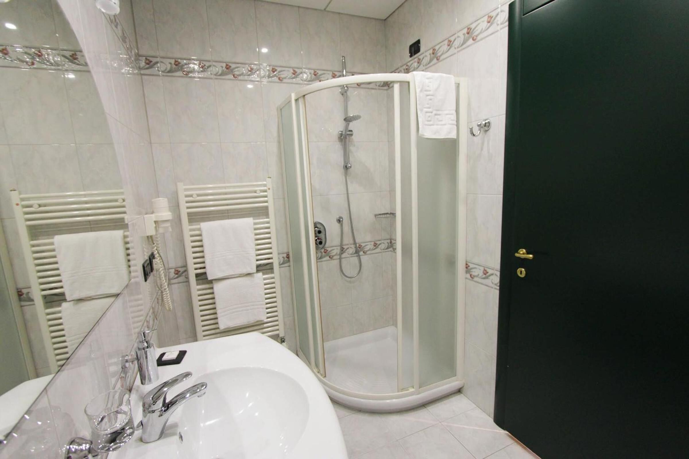 Un baño moderno con ducha de vidrio, un lavabo blanco y una puerta negra.