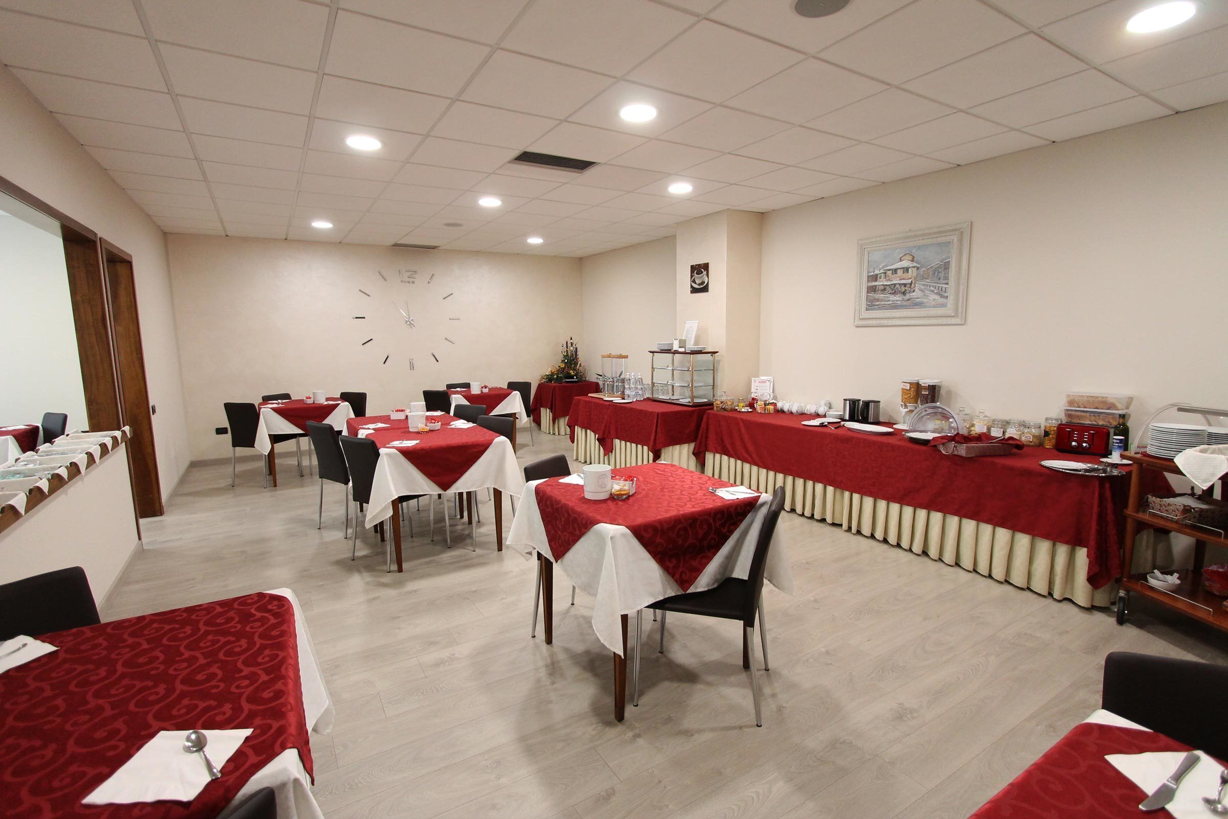 A conference room with multiple tables, each covered with a red tablecloth and white tablecloths, equipped with chairs and various items on the tables.