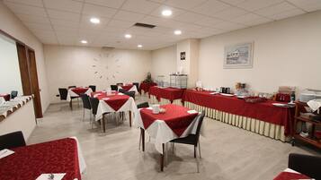 Un salón de conferencias con varias mesas, cada una cubierta con mantel rojo y blanco, equipado con sillas y distintos objetos sobre las mesas.