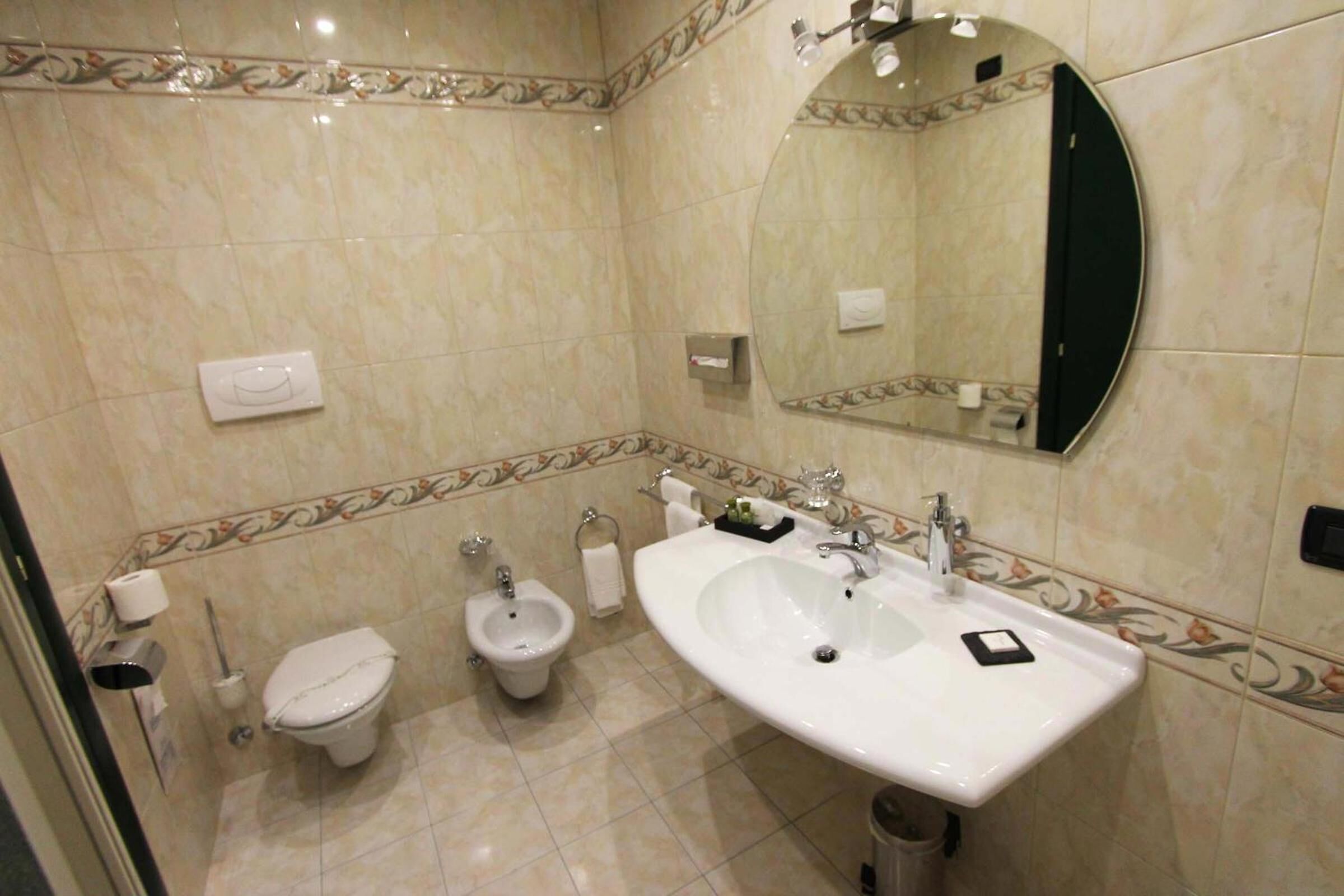 Une salle de bain équipée d’un WC, d’un bidet, d’un lavabo, d’un miroir et de carreaux décoratifs.