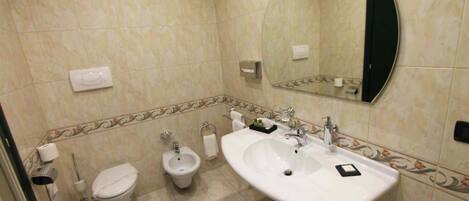 Ein Badezimmer mit Toilette, Bidet, Waschbecken, Spiegel und dekorativen Fliesen.