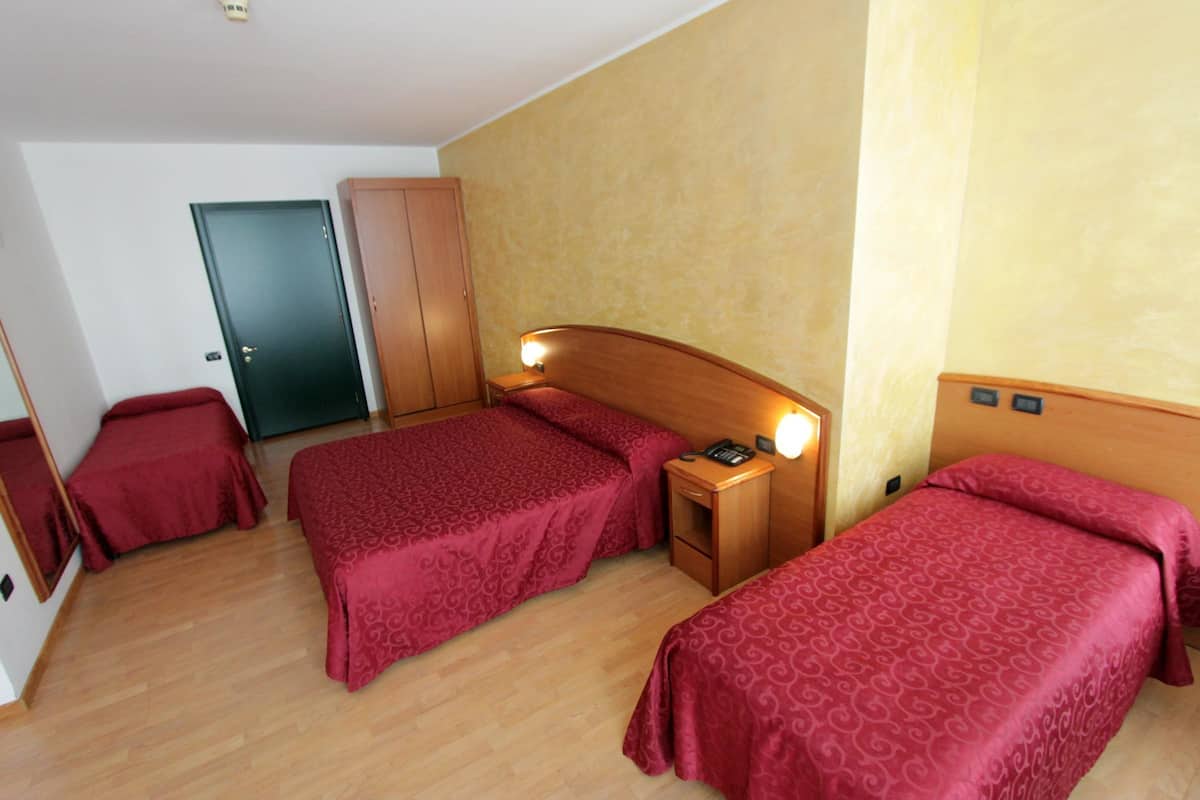 Ein Hotelzimmer mit zwei Einzelbetten, einem Holzschrank, einem Nachttisch mit Lampe und einer Tür.