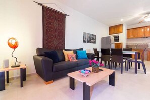 Un salon moderne avec un canapé noir, une table basse et un coin repas comprenant des chaises et une table en bois.