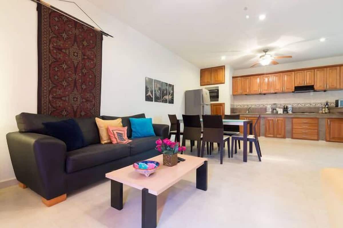 Una sala de estar moderna con un sofá negro, una mesa de centro y un comedor con sillas y una mesa.