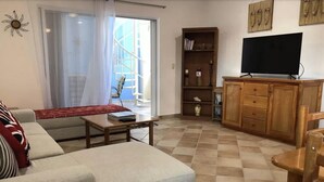Een woonkamer met een bank, salontafel, een tv op een houten kast en een boekenkast.