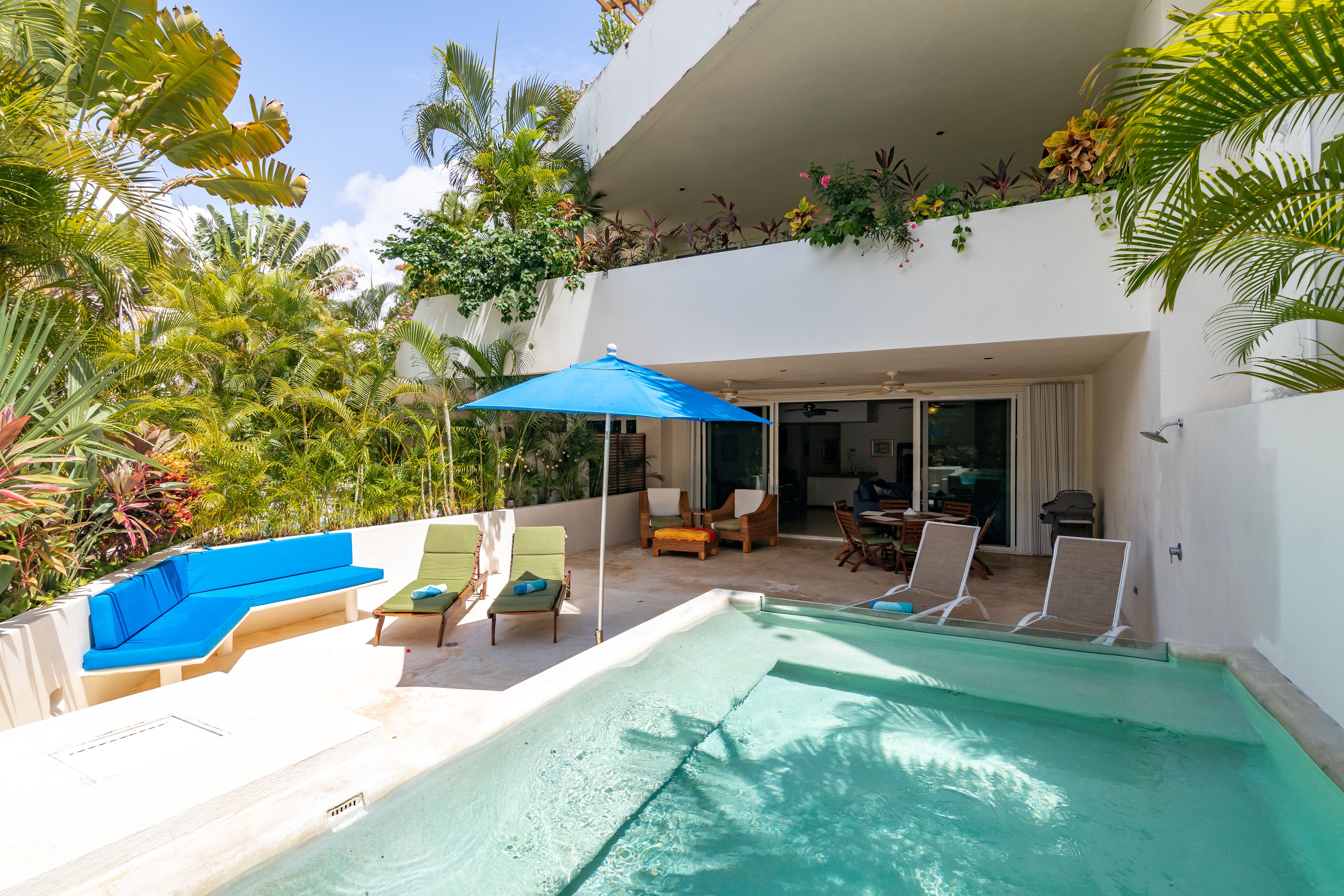 Un espace piscine avec des chaises longues, un parasol bleu et un coin salon abrité.