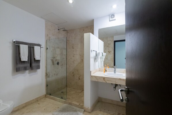 A modern bathroom with a glass shower enclosure, a white sink, and a large mirror. - Bosque de los Aluxes Condos with private pool by PPR (Playa del Carmen)