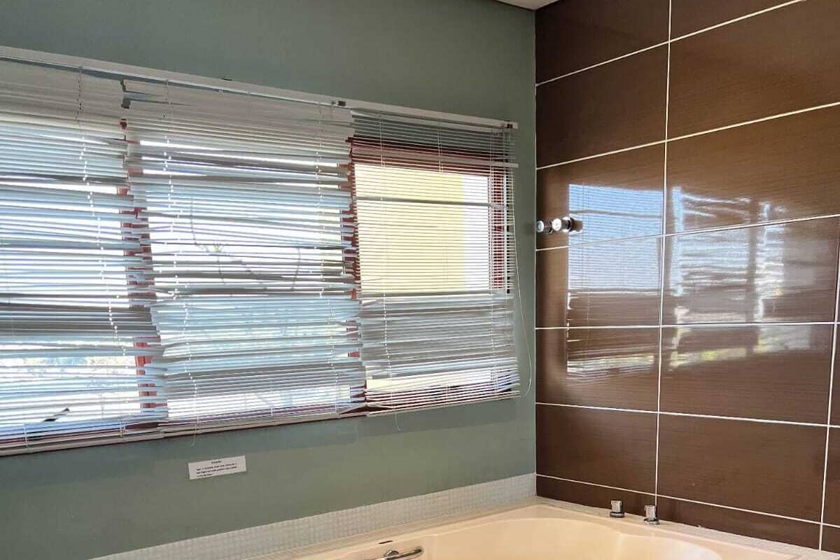Un baño moderno con una bañera grande, un perchero para toallas y una ventana con persianas.