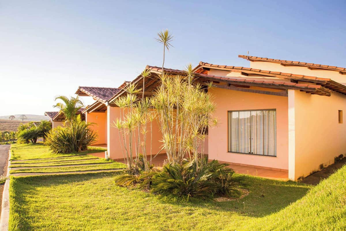 Una casa de un piso con techo de tejas, césped bien cuidado y una variedad de plantas tropicales.
