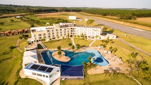 A large hotel with multiple floors, a swimming pool, and a road in the background. - Ramada by Wyndham Furnaspark (Formiga)