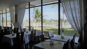 A restaurant with large windows, tables set with white tablecloths, and chairs. - Ramada by Wyndham Furnaspark (Formiga)