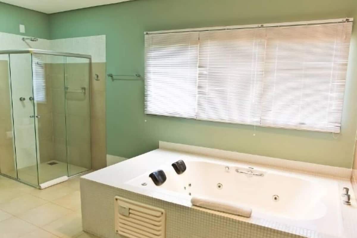 Un baño con ducha acristalada, una bañera grande y una ventana con persianas.