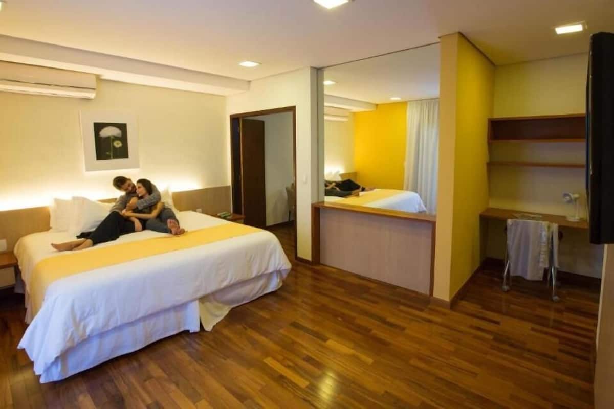 Habitación de hotel con dos camas, piso de madera, baño con espejo y un escritorio pequeño.