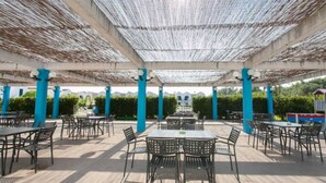 An outdoor patio area with tables and chairs, covered by a woven ceiling, and surrounded by blue pillars. - Blumare Hotel & Residence (Otranto)