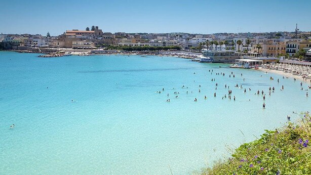 A coastal town with a clear blue sea, a beach with people, and buildings in the background. - Blumare Hotel & Residence (Otranto)