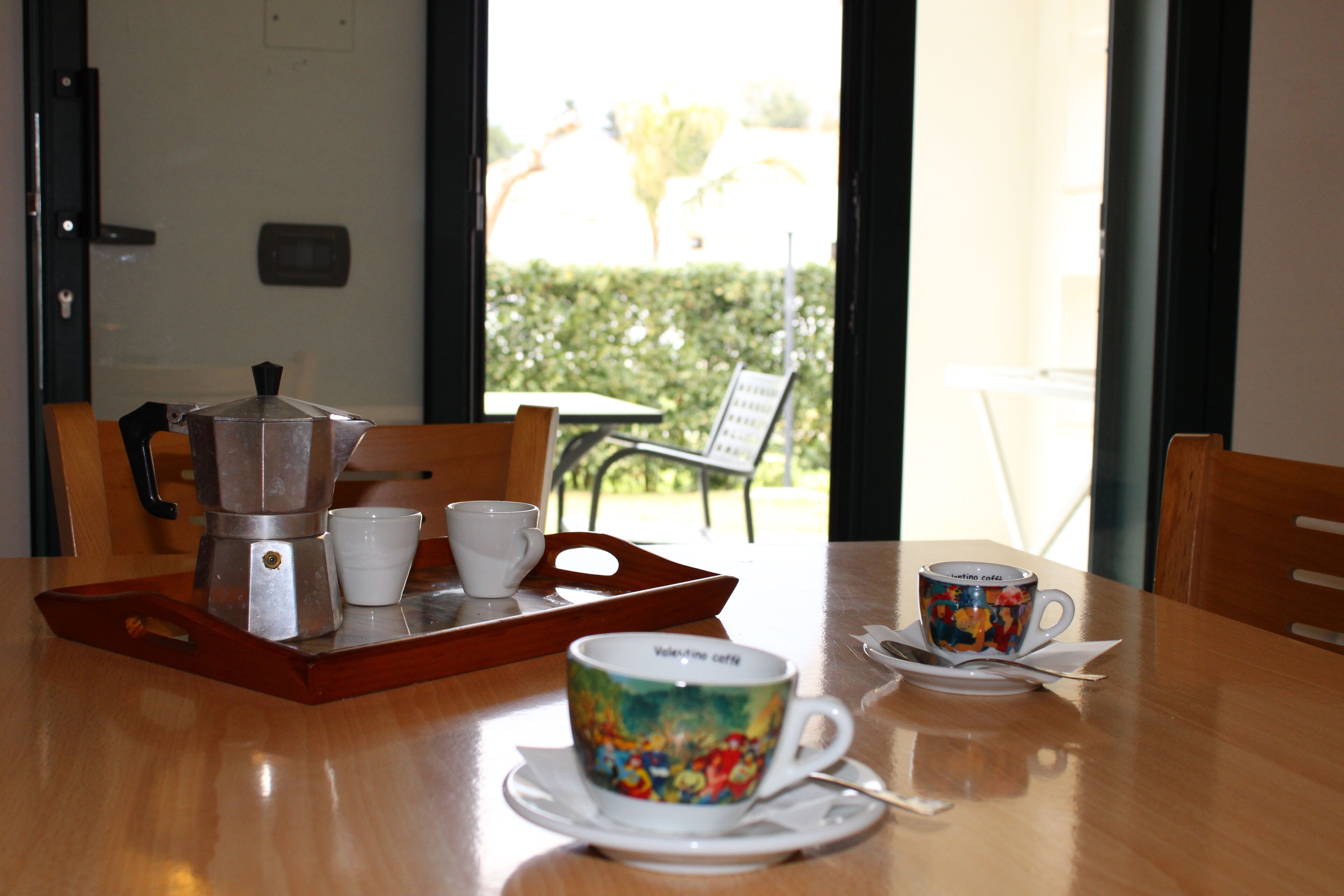 A dining table with a coffee maker, cups, and a colorful mug.