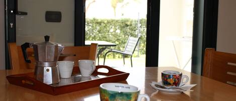 A dining table with a coffee maker, cups, and a colorful mug.