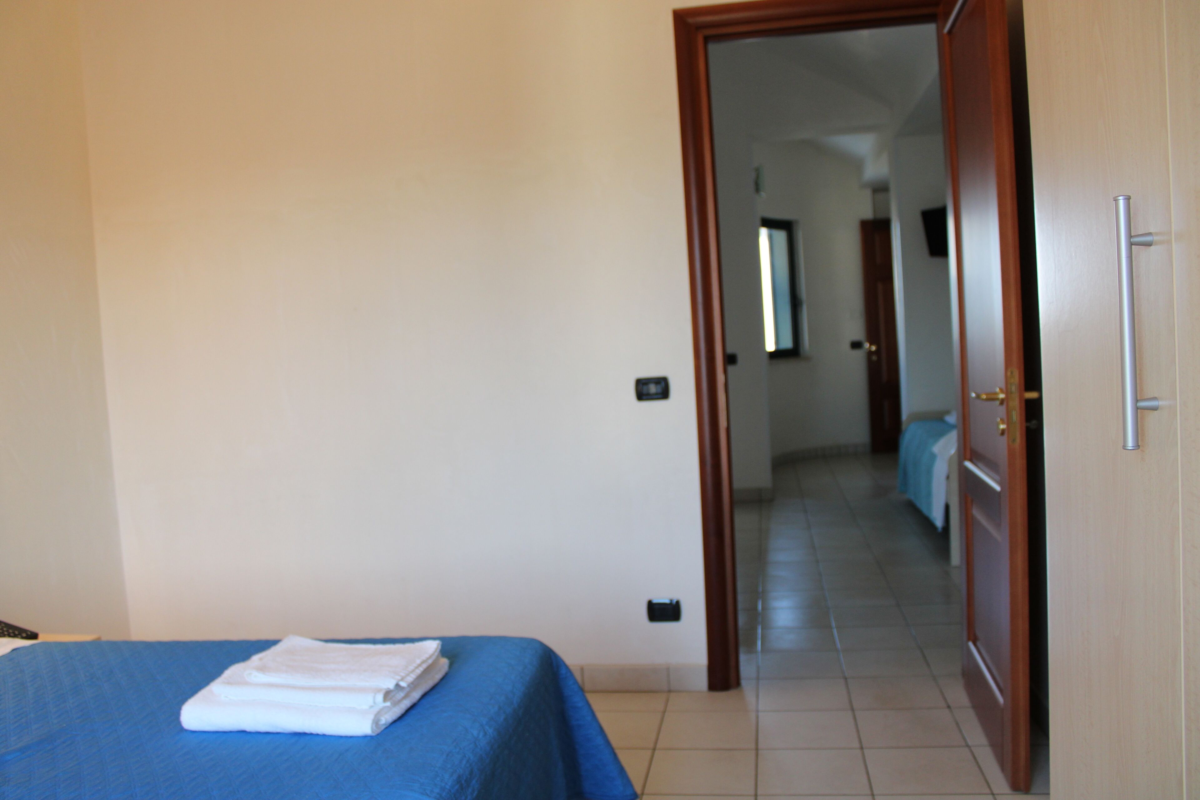 A hotel room with a bed, a blue bedspread, and a door leading to a hallway.