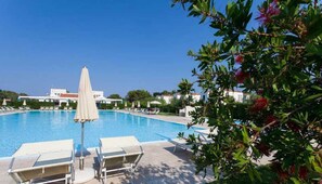 A swimming pool with lounge chairs and umbrellas, surrounded by greenery and buildings in the background. - Blumare Hotel & Residence (Otranto)