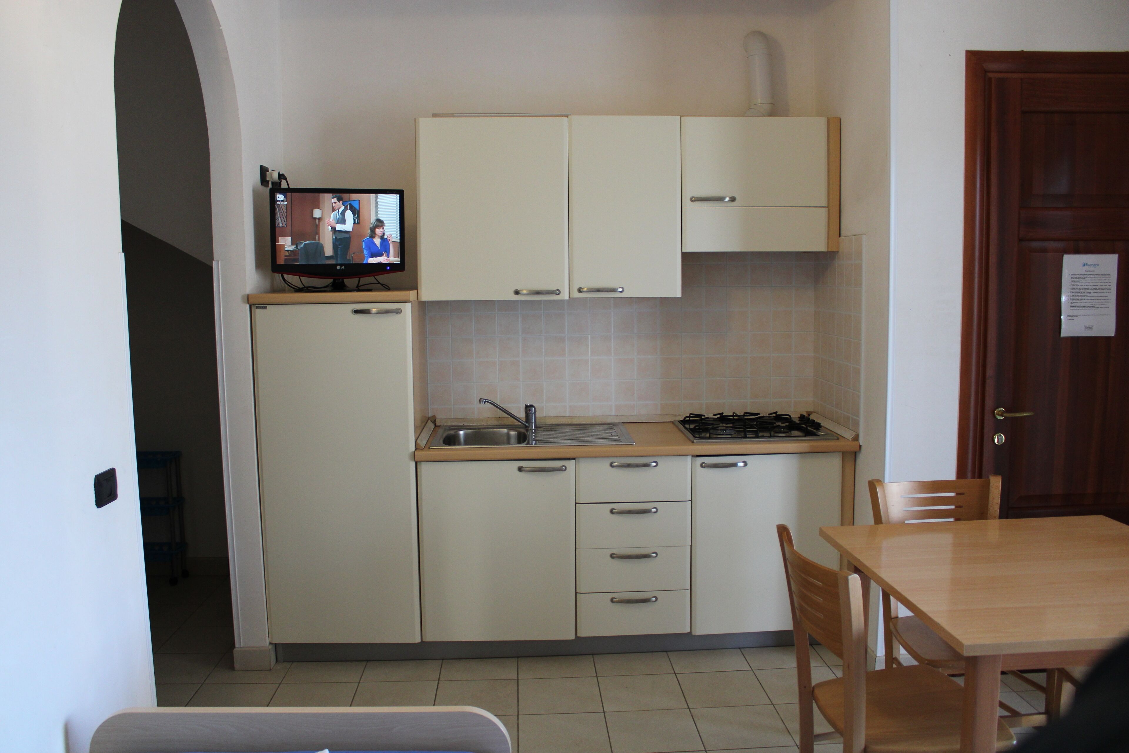 A compact kitchen with a TV, a sink, cabinets, and a dining area.
