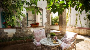 A rustic outdoor seating area with wicker chairs and a round table, surrounded by potted plants and a stone wall. - Hotel Bell Repos (Castell-Platja d'Aro)